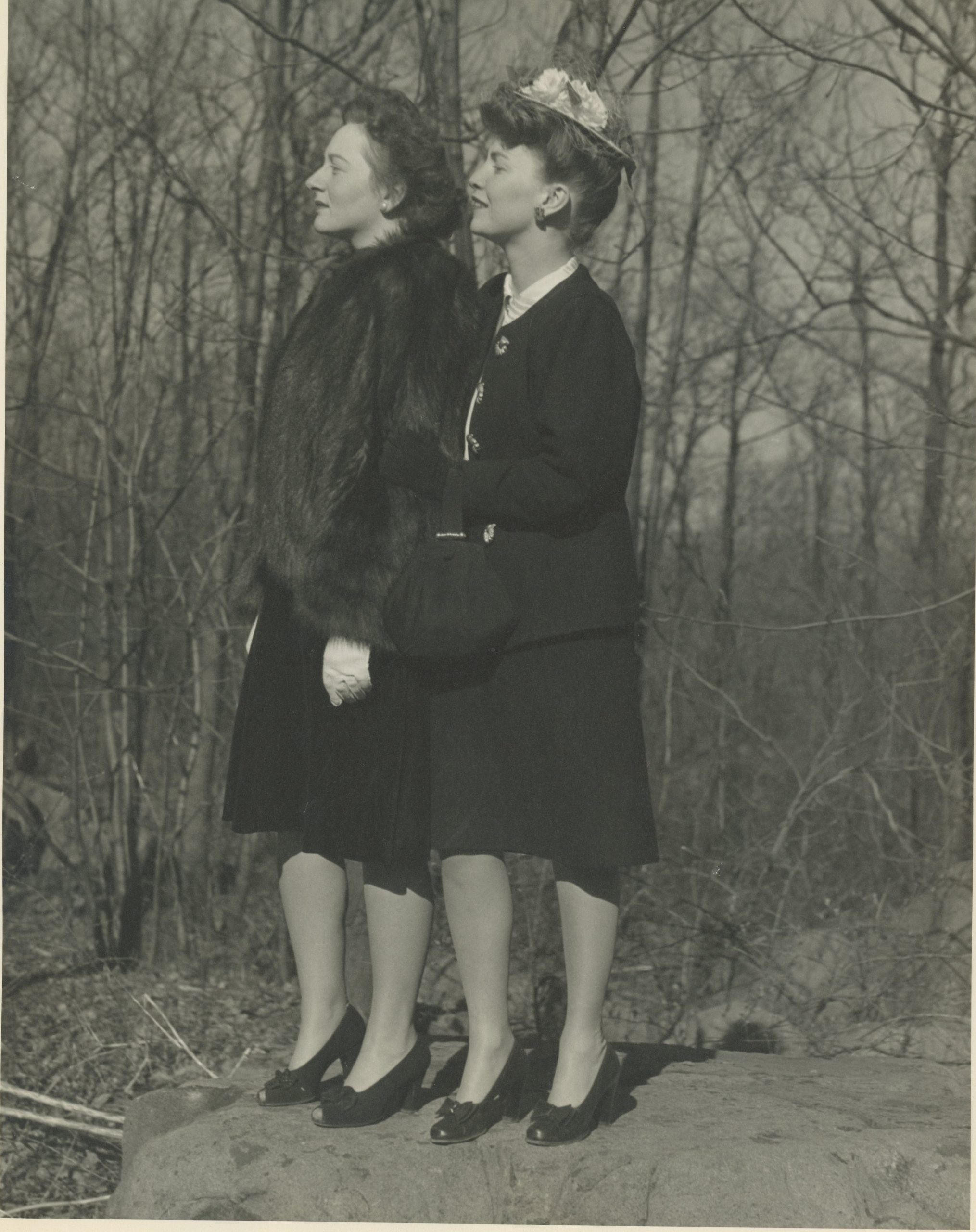 Photograph of two women standing together in front of a group of trees